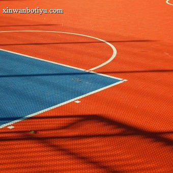 A vibrant sports court with sections of red and blue, featuring crisp white lines marking the boundaries. Shadows from a structure create geometric patterns across the surface, adding depth and interest to the scene.